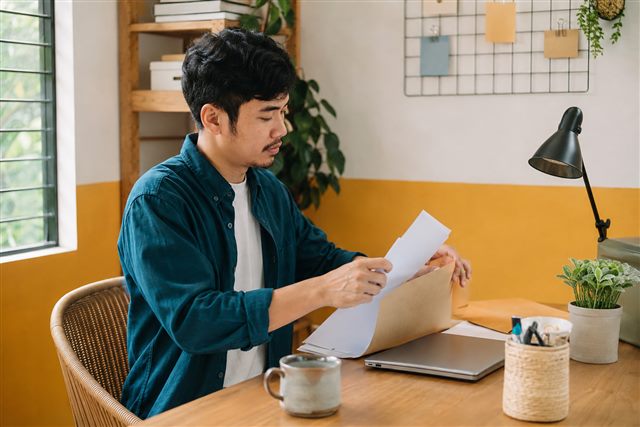 A man organizing papers into a folder at his home workspace